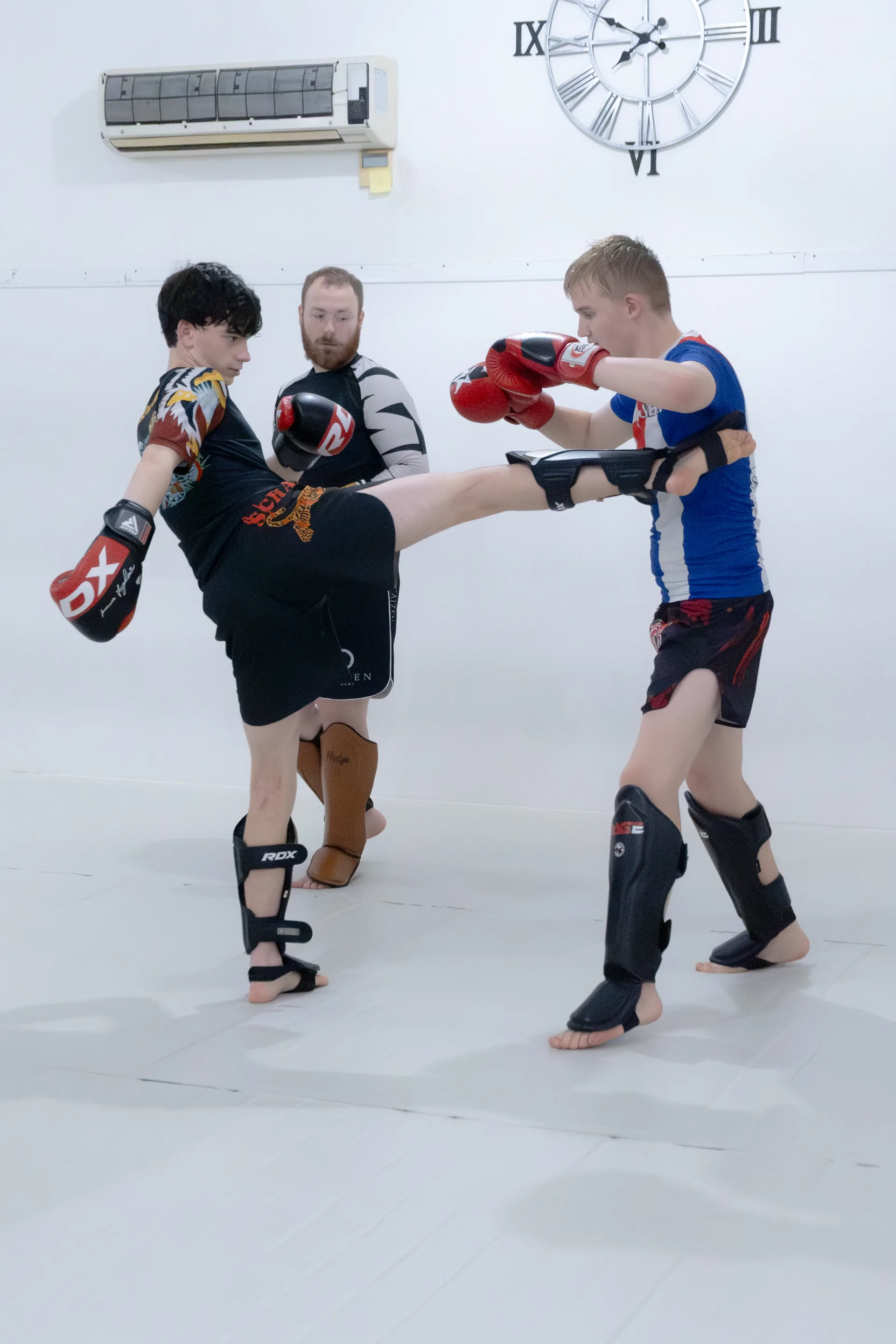Kickboxing partners practising a kick with a coach watching