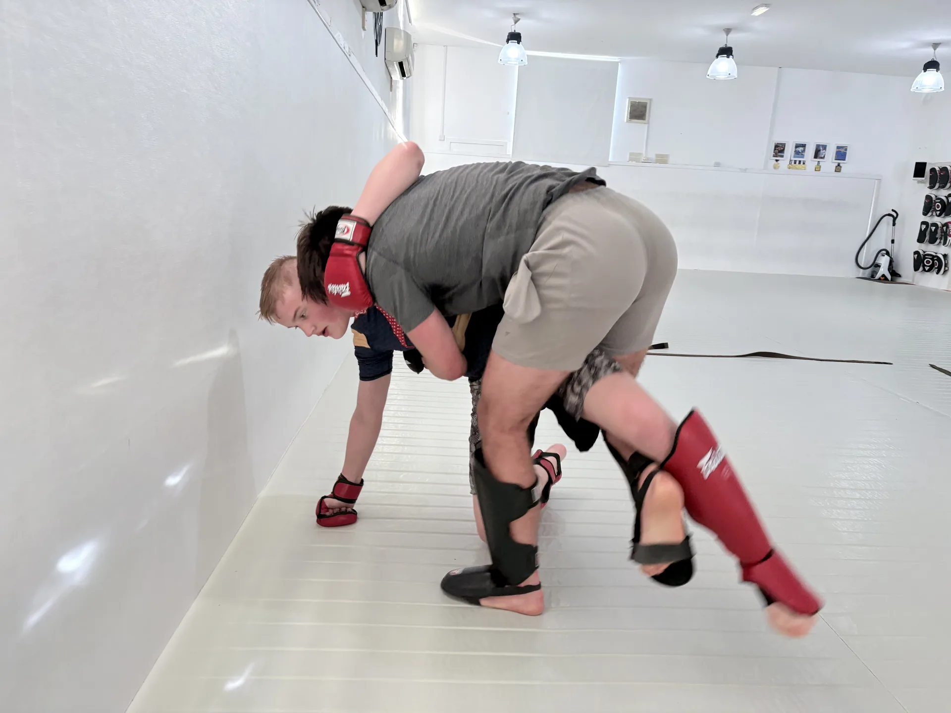Two members practising an MMA grappling position beside the training wall